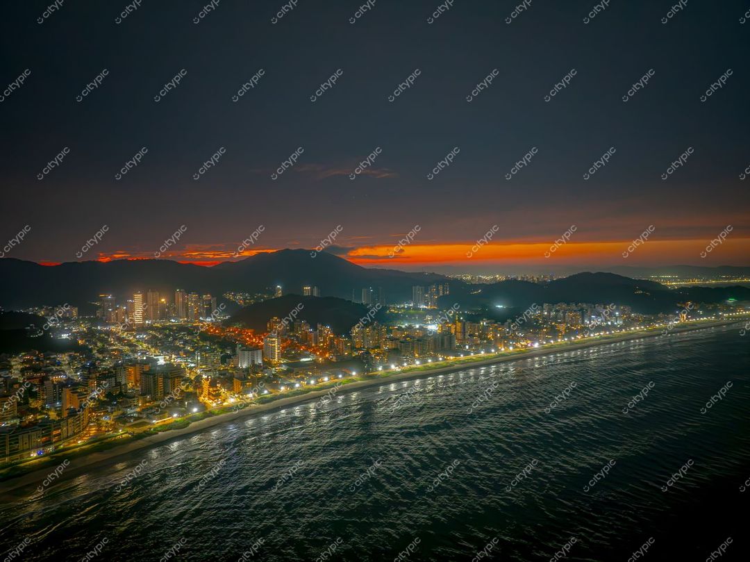 Itajaí, Santa Catarina, crepúsculo com reflexos quentes no mar e edifícios iluminados à beira da praia