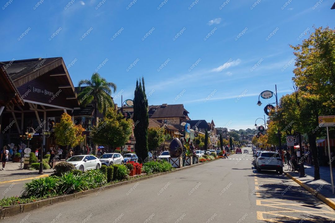 Gramado, Rio Grande do Sul, rua movimentada com arquitetura europeia e vegetação exuberante sob céu ensolarado