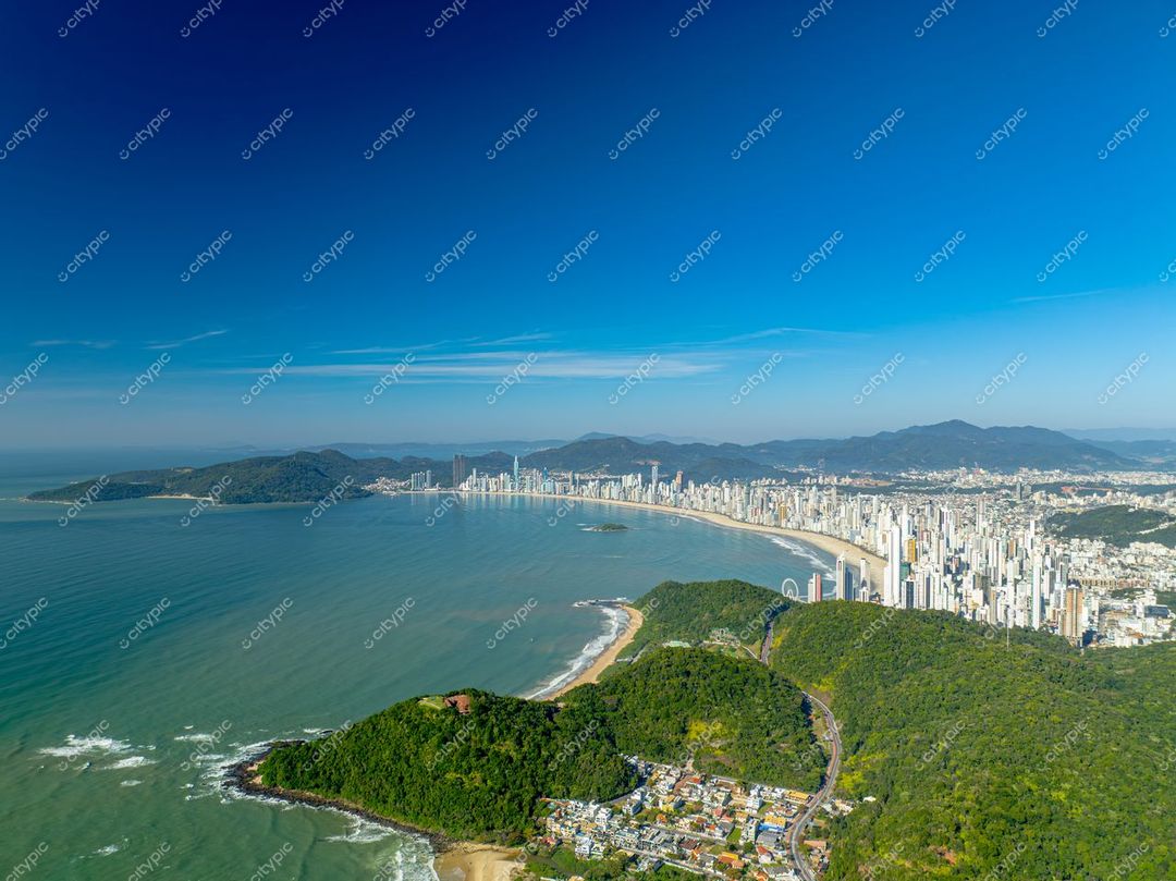 Itajaí, Santa Catarina vista aérea com vegetação densa à esquerda e arranha-céus modernos à direita sob céu azul claro