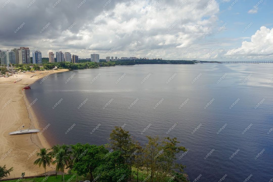 Manaus, Amazonas vista panorâmica da orla com faixa de areia e edifícios entre vegetação tropical sob céu nublado