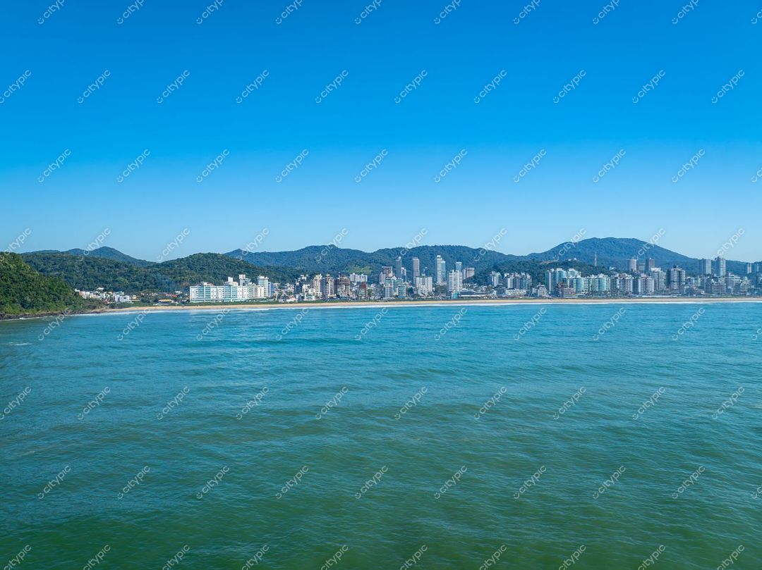 Itajaí, Santa Catarina vista panorâmica com edifícios modernos à beira-mar e montanhas suaves ao fundo em dia ensolarado