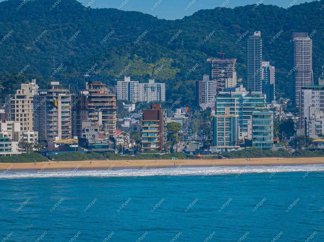Itajaí, Santa Catarina vista da costa com prédios modernos, vegetação montanhosa e praia extensa em dia ensolarado