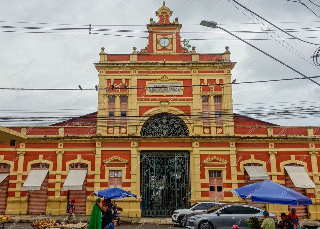Manaus, Amazonas, edificação histórica com fachada vermelha e amarela sob céu nublado e barracas de vendedores nas proximidades
