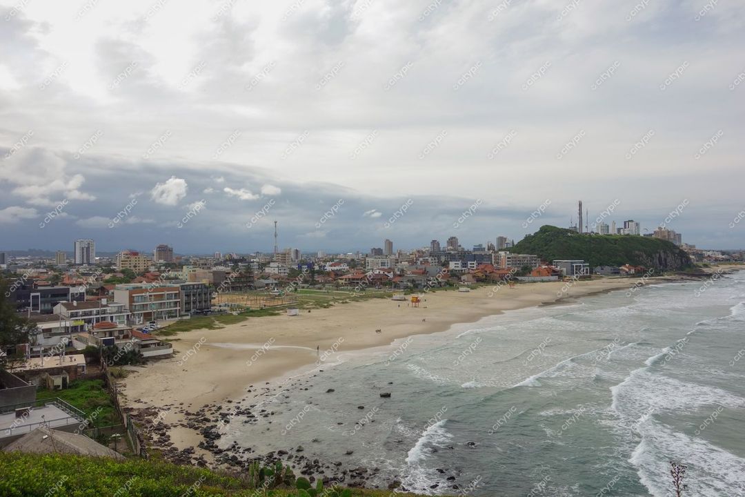 Torres, Rio Grande do Sul, praia com areia clara e rochas, céu nublado e água agitada ao fundo urbano