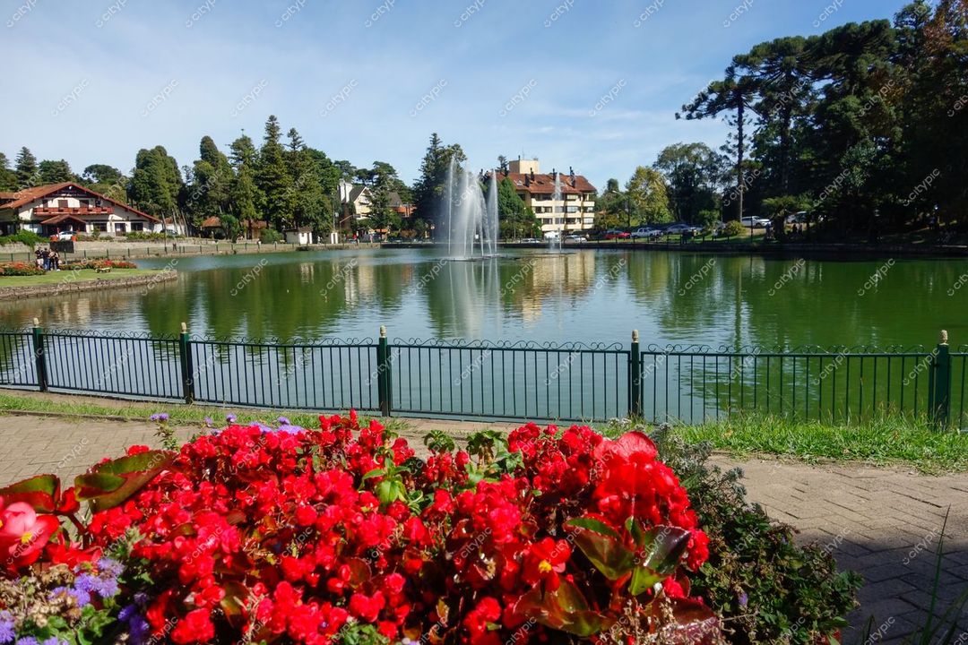 Gramado, Rio Grande do Sul, lago tranquilo com fonte central e flores vermelhas em canteiros vibrantes sob céu ensolarado