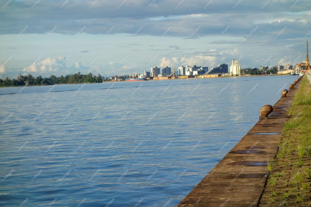 Porto Alegre, Rio Grande do Sul, pôr do sol refletido no rio com vegetação e prédios ao fundo