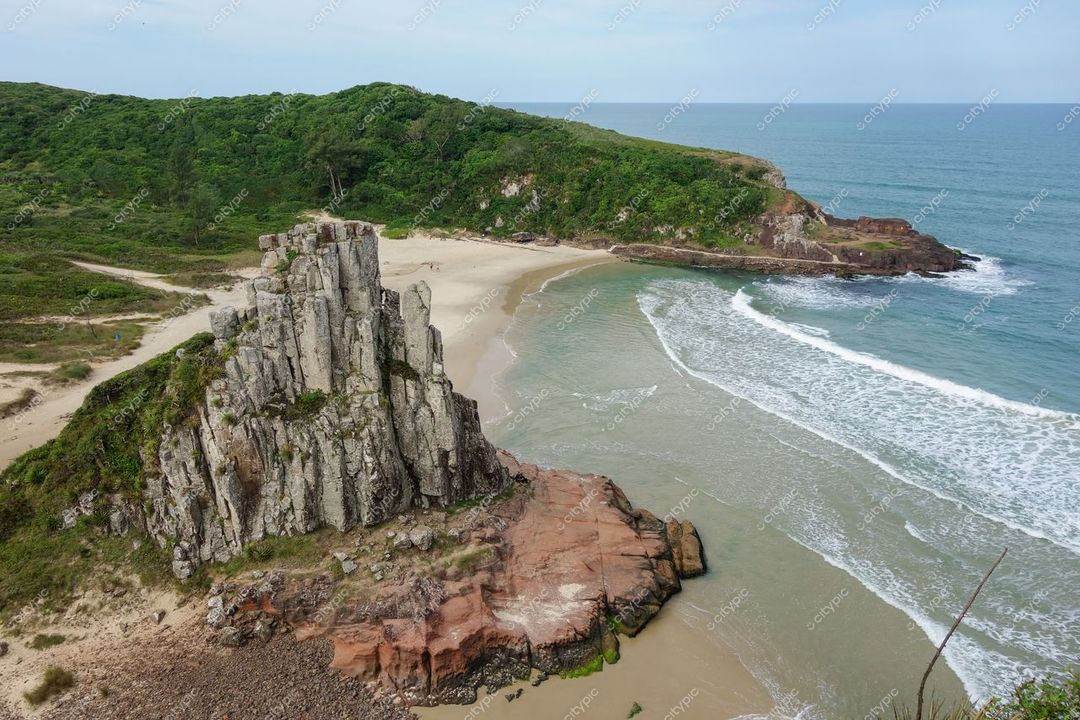 Torres, Rio Grande do Sul, formação rochosa à beira da praia com vegetação densa e céu claro em dia ensolarado