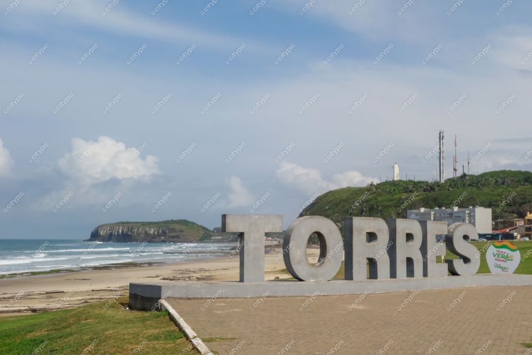 Torres, Rio Grande do Sul com letreiro em primeiro plano e costa verdejante sob céu com nuvens brancas