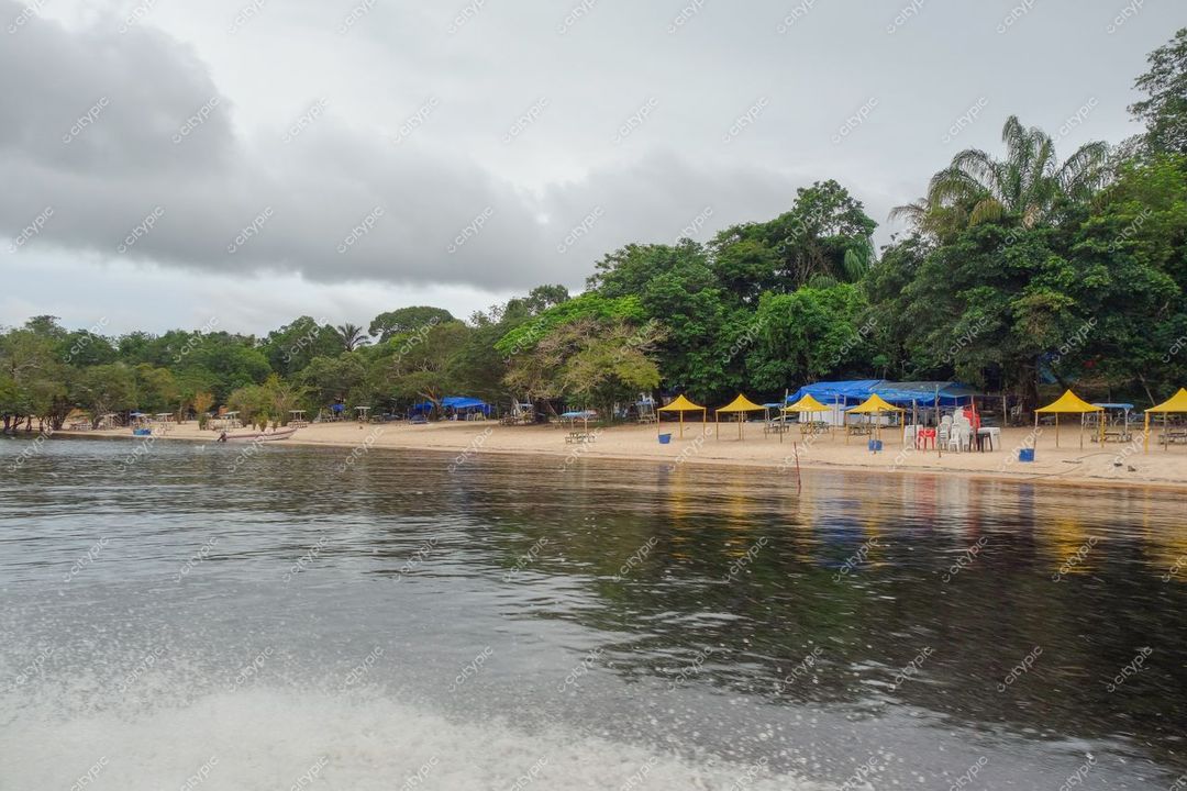 Manaus, Amazonas, praia com areia clara e barracas coloridas sob céu nublado e vegetação densa ao fundo