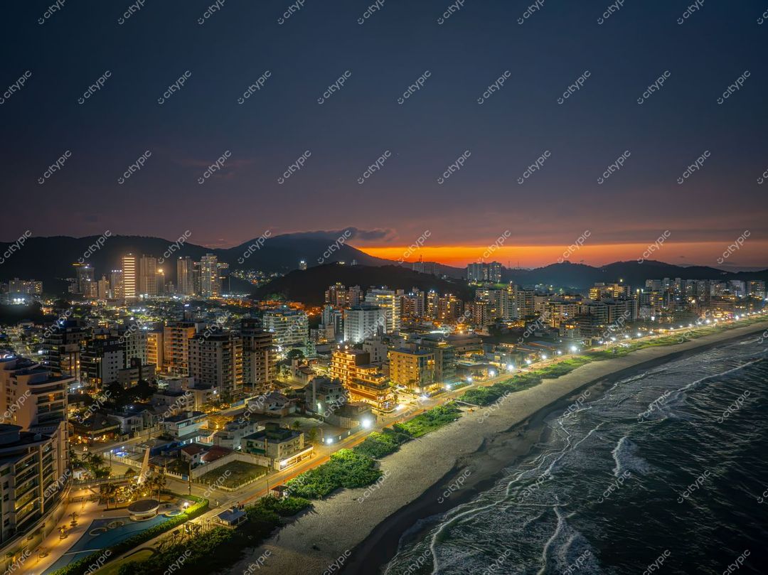 Itajaí, Santa Catarina vista noturna com cidade iluminada à esquerda e praia de areia à direita ao pôr do sol
