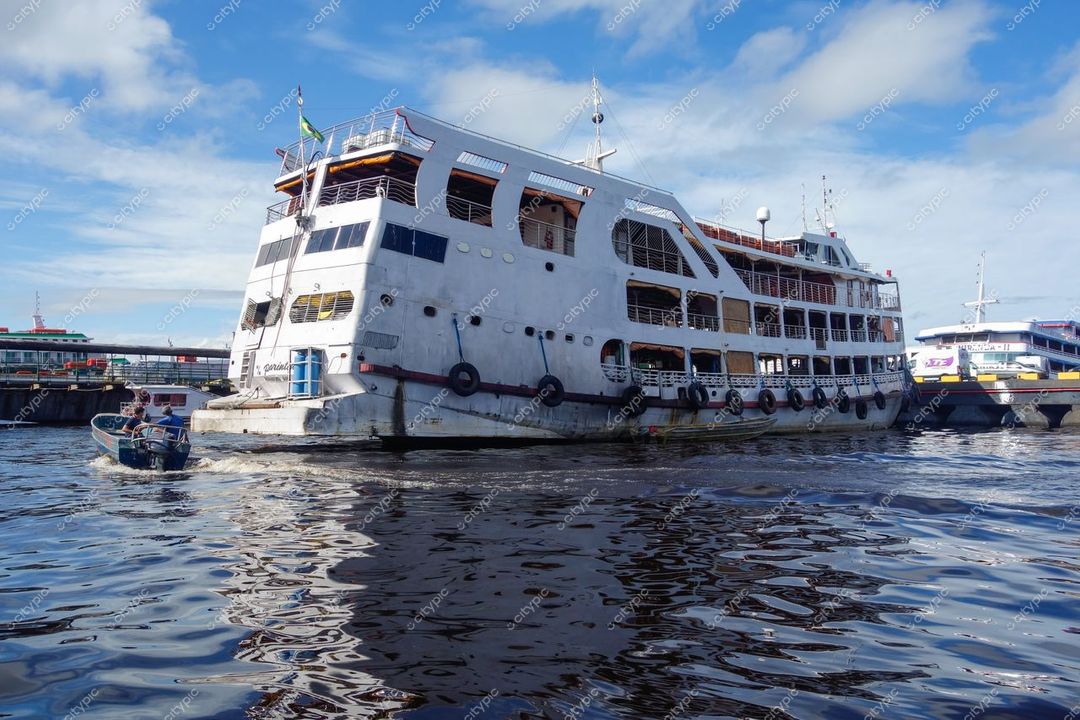 Manaus, Amazonas, embarcação de grande porte inclinada ancorada em porto com céu claro e vegetação tropical ao fundo