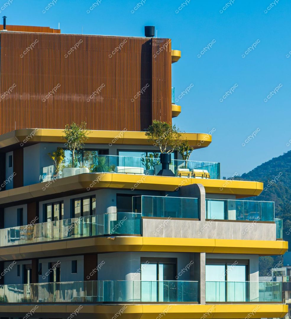 Itajaí, Santa Catarina, moderno edifício com varandas de vidro e detalhes em amarelo sob céu azul claro e montanhas ao fundo