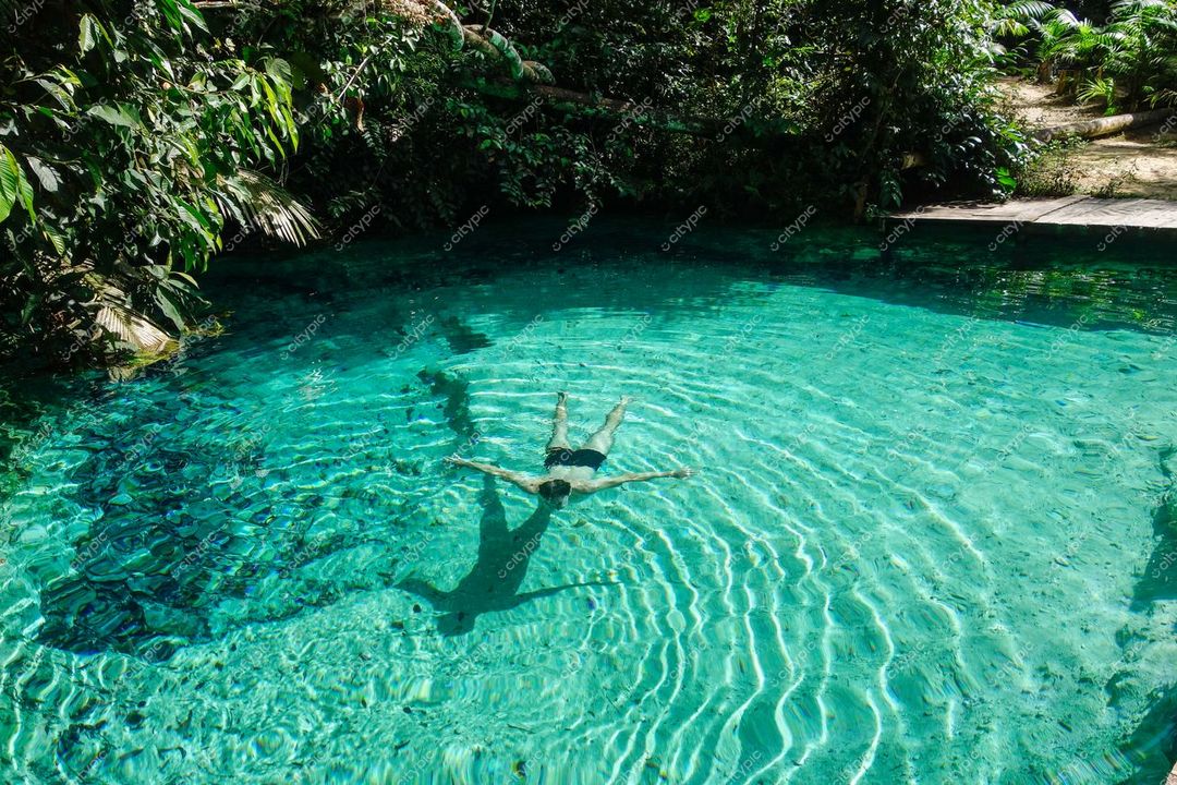 Presidente Figueiredo, Amazonas, pessoa flutuando em piscina natural com vegetação exuberante e luz do sol refletida na água