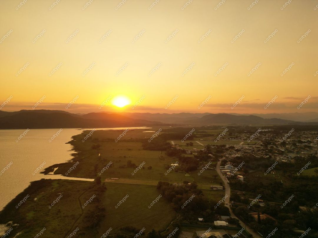 Lagoa do Mirim em Imbituba com pôr do sol iluminando água e montanhas, áreas verdes e pequenas construções