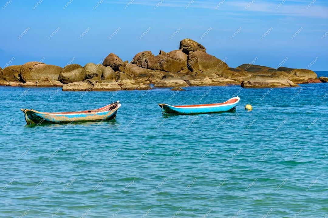 Ilhabela, São Paulo, canoas à deriva em águas calmas com rochas ao fundo e céu azul claro