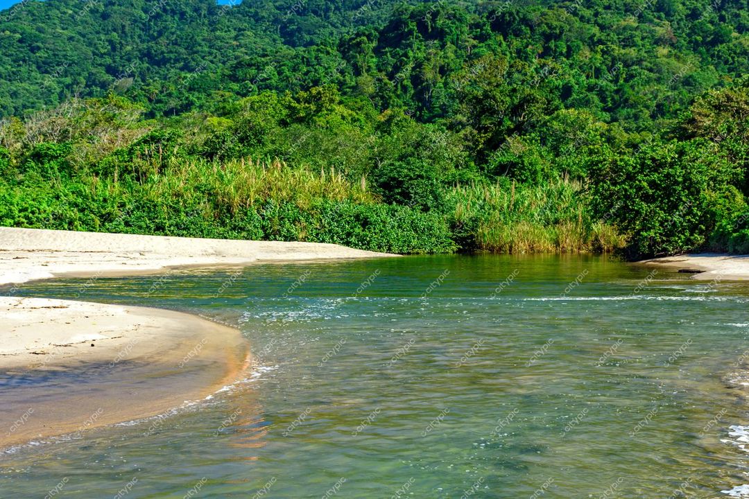 Ilhabela, São Paulo, leito de rio sereno encontrando praia de areia clara cercada por vegetação densa e montanhas