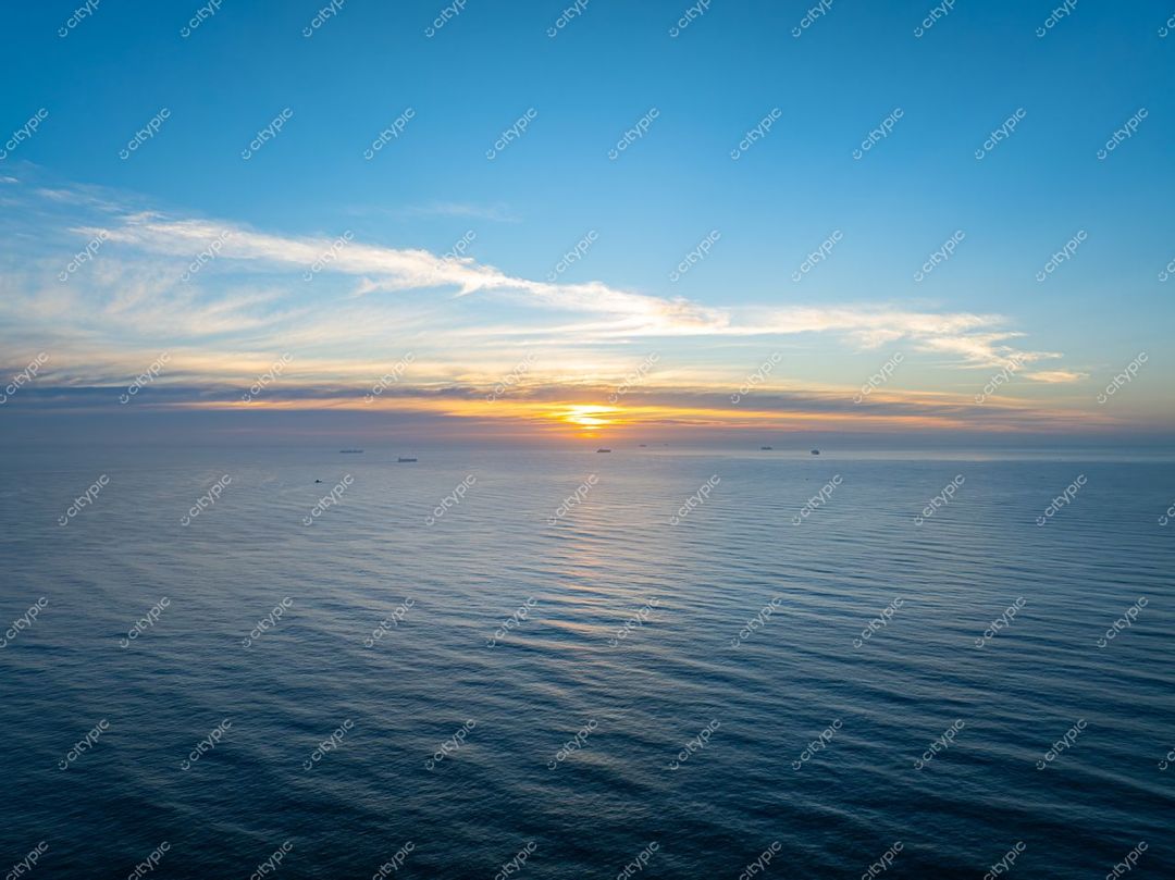 Itajaí, Santa Catarina, pôr do sol sereno com céu azul e laranja refletido no mar calmo e navios ao fundo