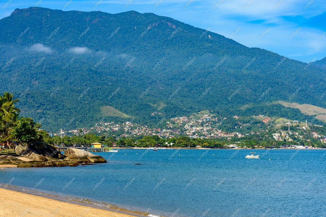 Ilhabela, São Paulo vista da praia em dia ensolarado com vegetação montanhosa e barcos pequenos na água calma