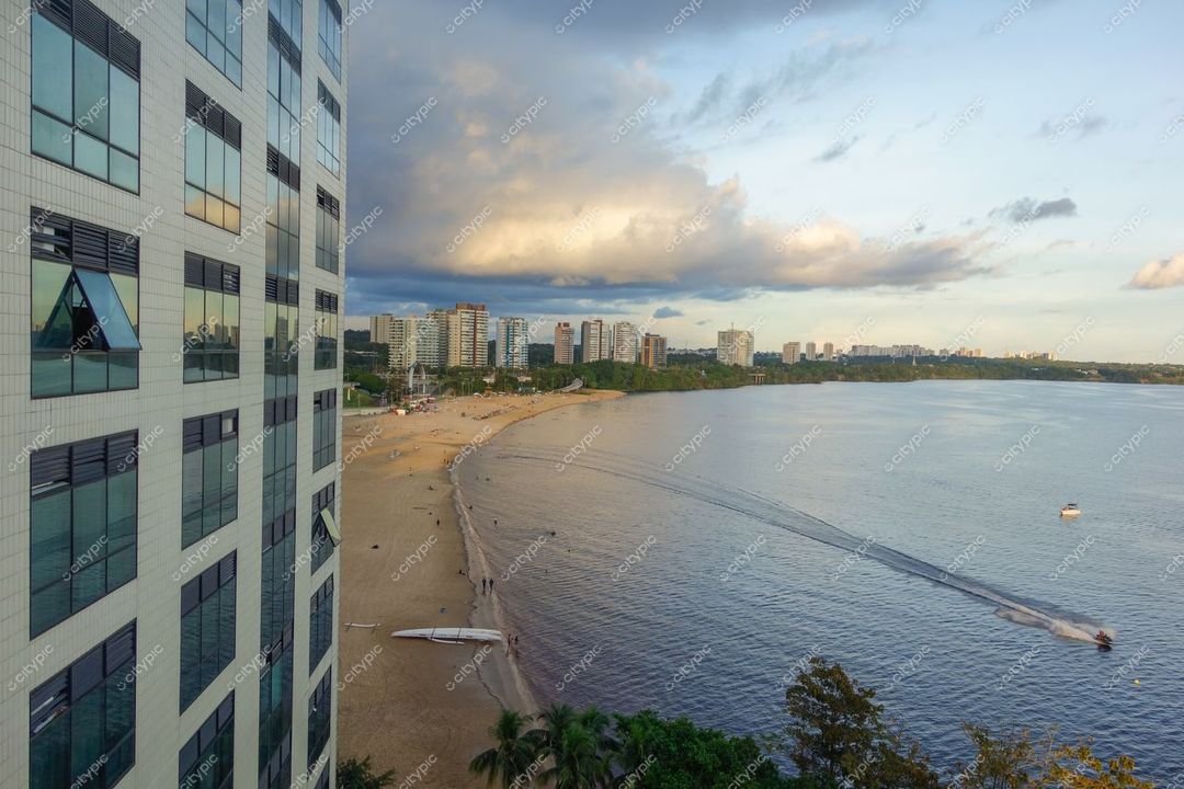 Manaus, Amazonas, vista panorâmica da orla com edifício em primeiro plano e reflexos do pôr do sol no rio